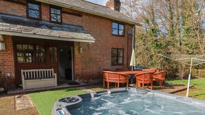 A hot tub in a backyard with a brick house, a wooden bench, and a table with chairs.
