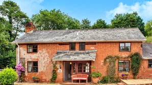A brick house with a front porch, a bench, and potted plants.