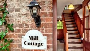 A brick wall with a sign reading "Mill Cottage" and a staircase leading inside.