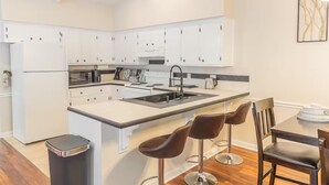 Une cuisine moderne avec des meubles blancs, un îlot central et un coin repas équipé de deux tabourets de bar.