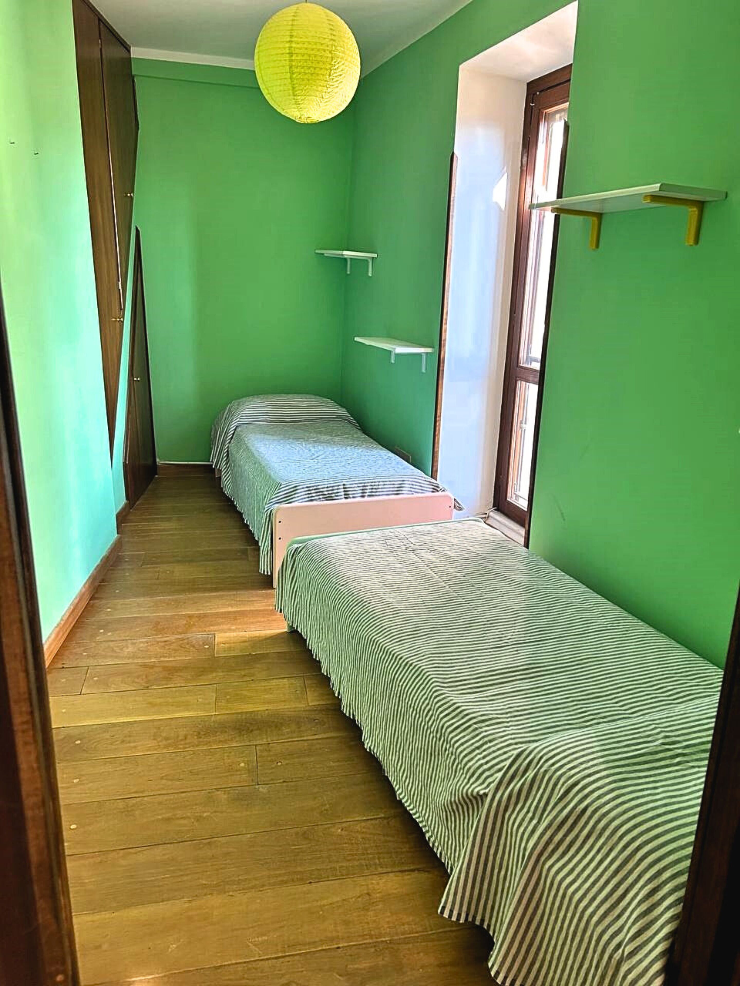 A narrow hallway with two single beds, wooden flooring, and green walls.