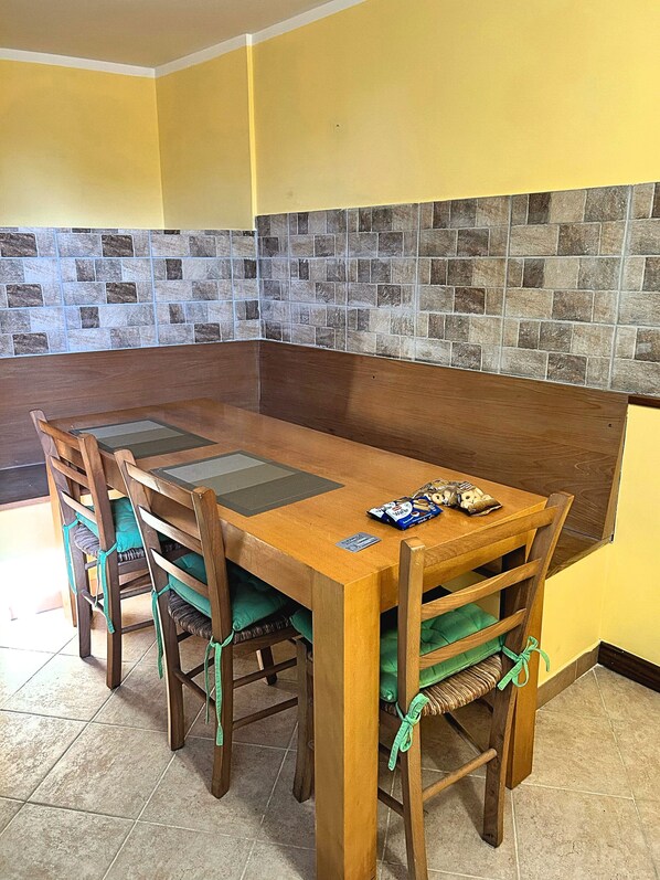 A dining area with a wooden table and chairs, a tiled backsplash, and a yellow wall. - All'Orologio 2 Camere Terrazza Vista (San Donato Val Di Comino)