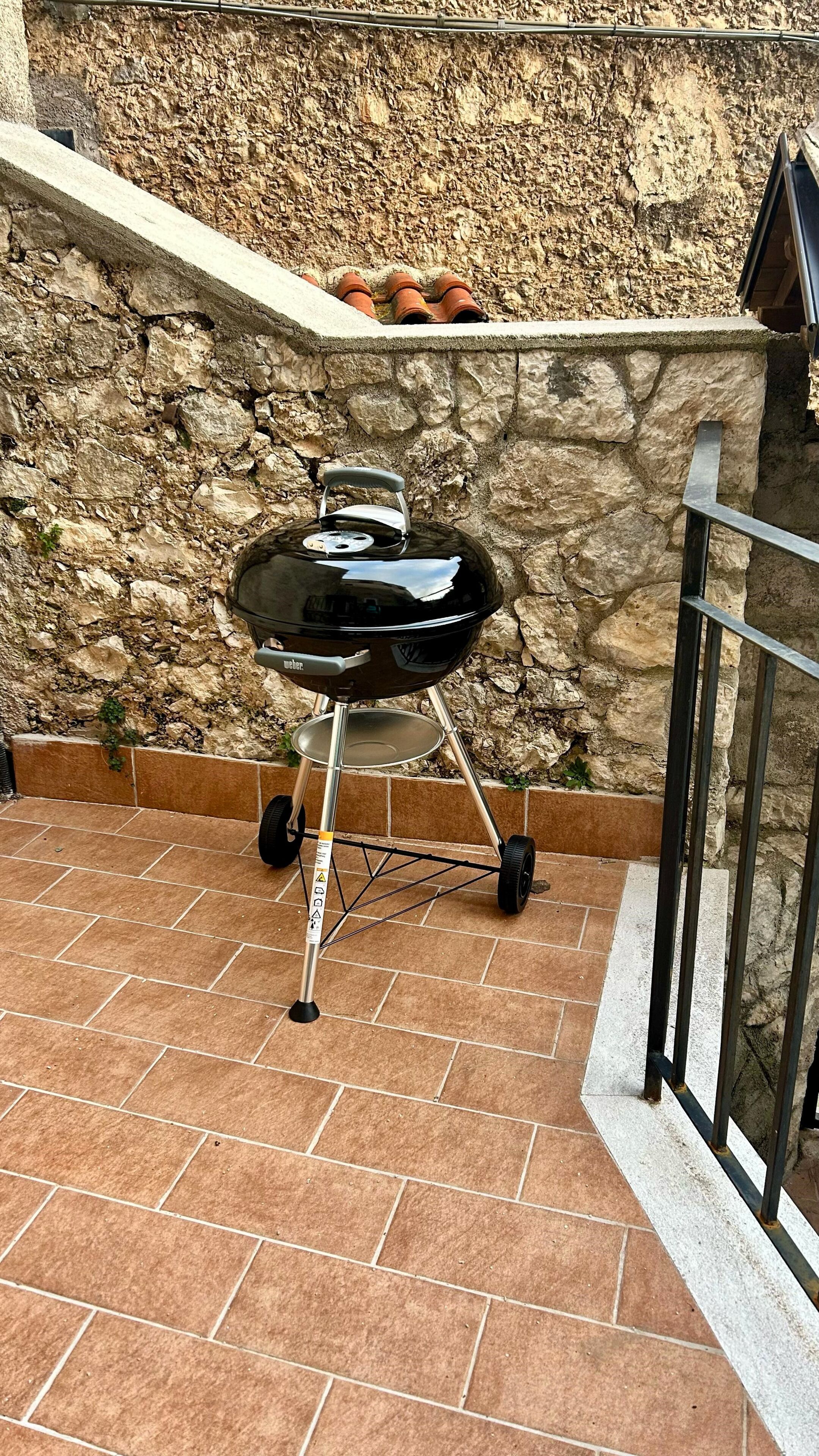 A black Weber grill on a tiled patio with a stone wall in the background.