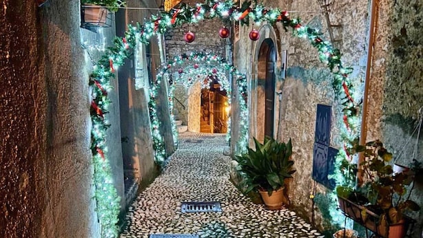 A narrow cobblestone alley with a decorative archway adorned with lights and greenery, leading to a building entrance. - All'Orologio 2 Camere Terrazza Vista (San Donato Val Di Comino)