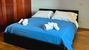 A neatly made bed with blue bedding and white pillows, wooden wardrobe, and a light switch on the wall. - All'Orologio 2 Camere Terrazza Vista (San Donato Val Di Comino)