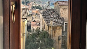 A view through a window of a town with historic buildings, a prominent church spire, and a mountainous backdrop. - All'Orologio 2 Camere Terrazza Vista (San Donato Val Di Comino)