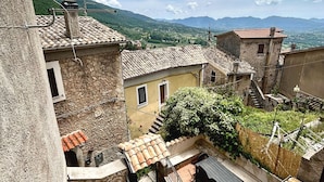 A courtyard with stone steps leading to a wooden deck, surrounded by traditional buildings with terracotta roofs. - All'Orologio 2 Camere Terrazza Vista (San Donato Val Di Comino)