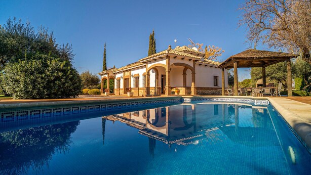 Una piscina con reflejo cristalino, un edificio con arcos y un pabellón.