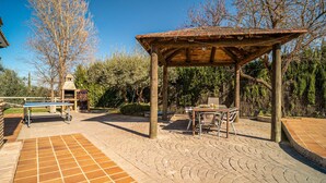 Un espacio de estar al aire libre cubierto con mesa y sillas, una parrilla de barbacoa y un patio empedrado.