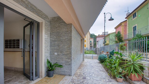 Un étroit sentier mène à un bâtiment doté d’une façade en pierre et d’une entrée avec une porte en verre.