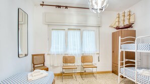 Une chambre à coucher comprenant un lit, deux chaises, une armoire, un lit superposé, un miroir et une maquette de bateau.