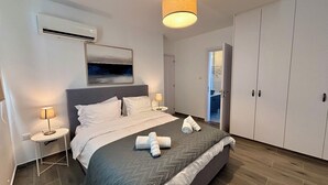 Quarto de hotel moderno com uma cama grande, uma mesa de cabeceira com abajur, um guarda-roupa e um quadro na parede.