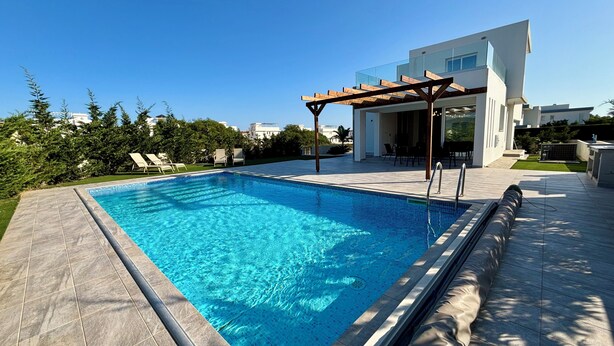 Piscina moderna com pérgola, cercada por um gramado bem cuidado e uma casa contemporânea.