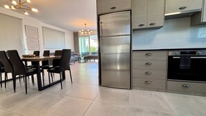 Cozinha moderna com geladeira de aço inoxidável, forno embutido e área de refeições com mesa e cadeiras.
