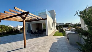 Uma área de estar moderna ao ar livre, com pergolado, assentos e um pequeno jardim.