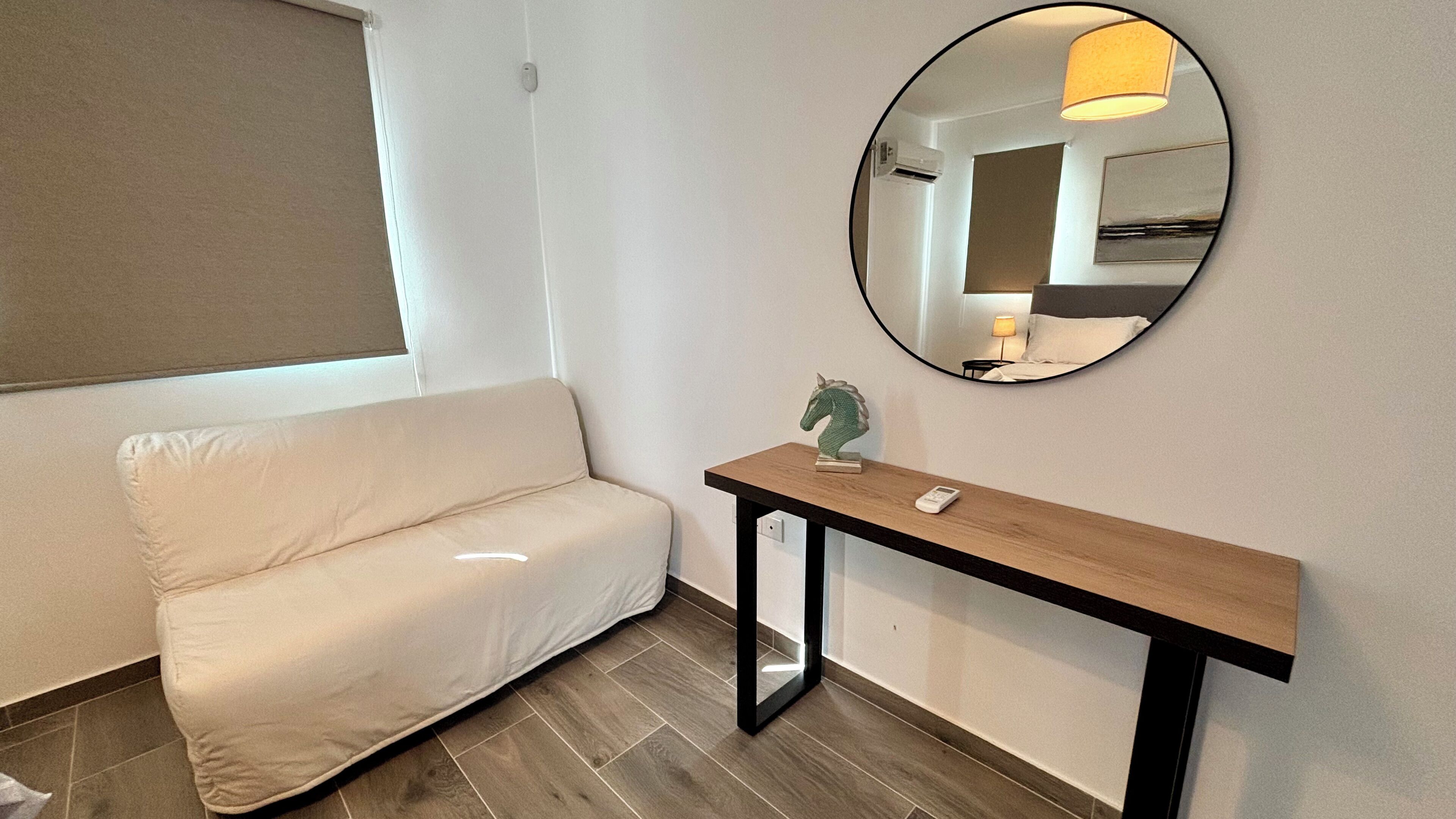 A modern hotel room with a sofa, a console table with a decorative horse head, and a round mirror on the wall.