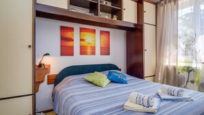 Een netjes opgemaakt bed met gestreepte lakens, twee kussens en opgevouwen handdoeken. Daarboven hangen drie schilderijen aan de muur.