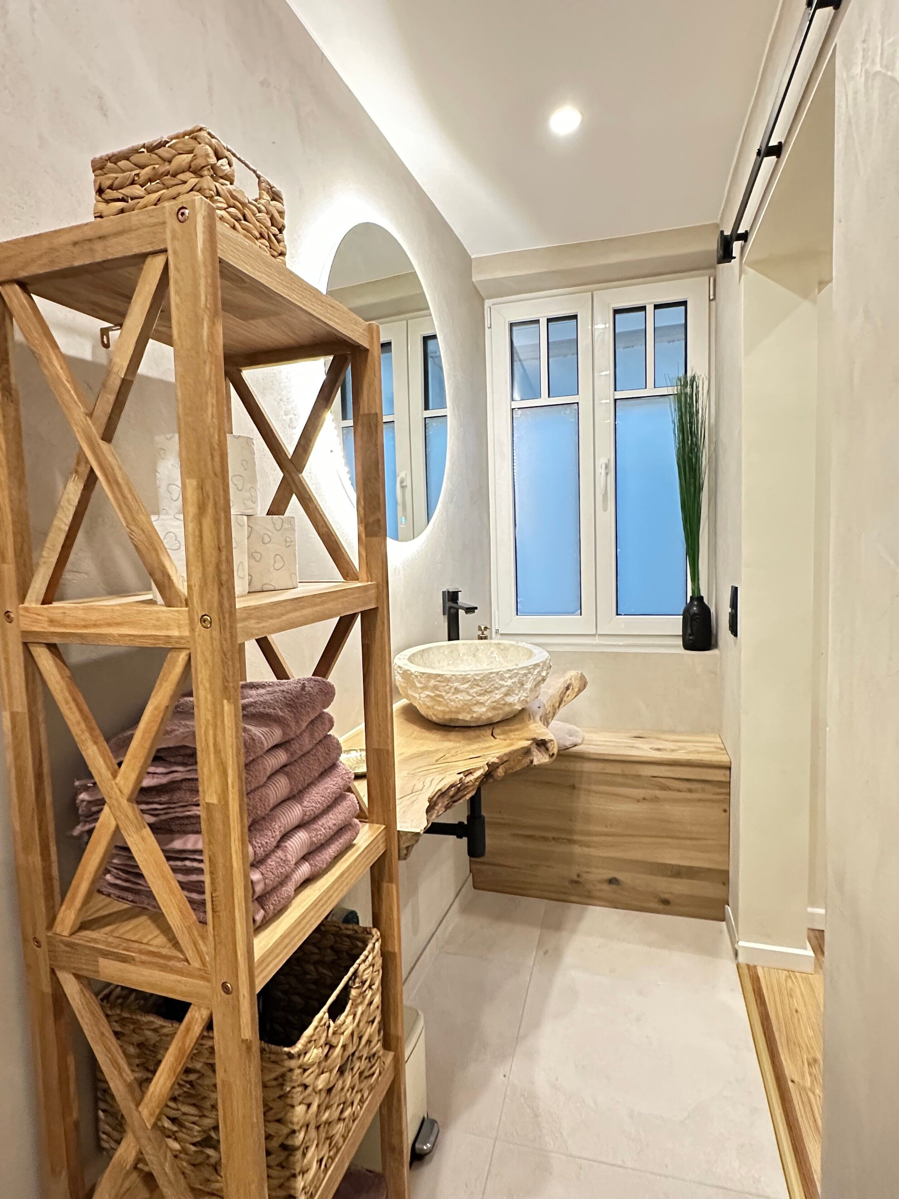 Ein Badezimmer mit Holzregal, Waschbecken, Fenster und Handtuchhalter.