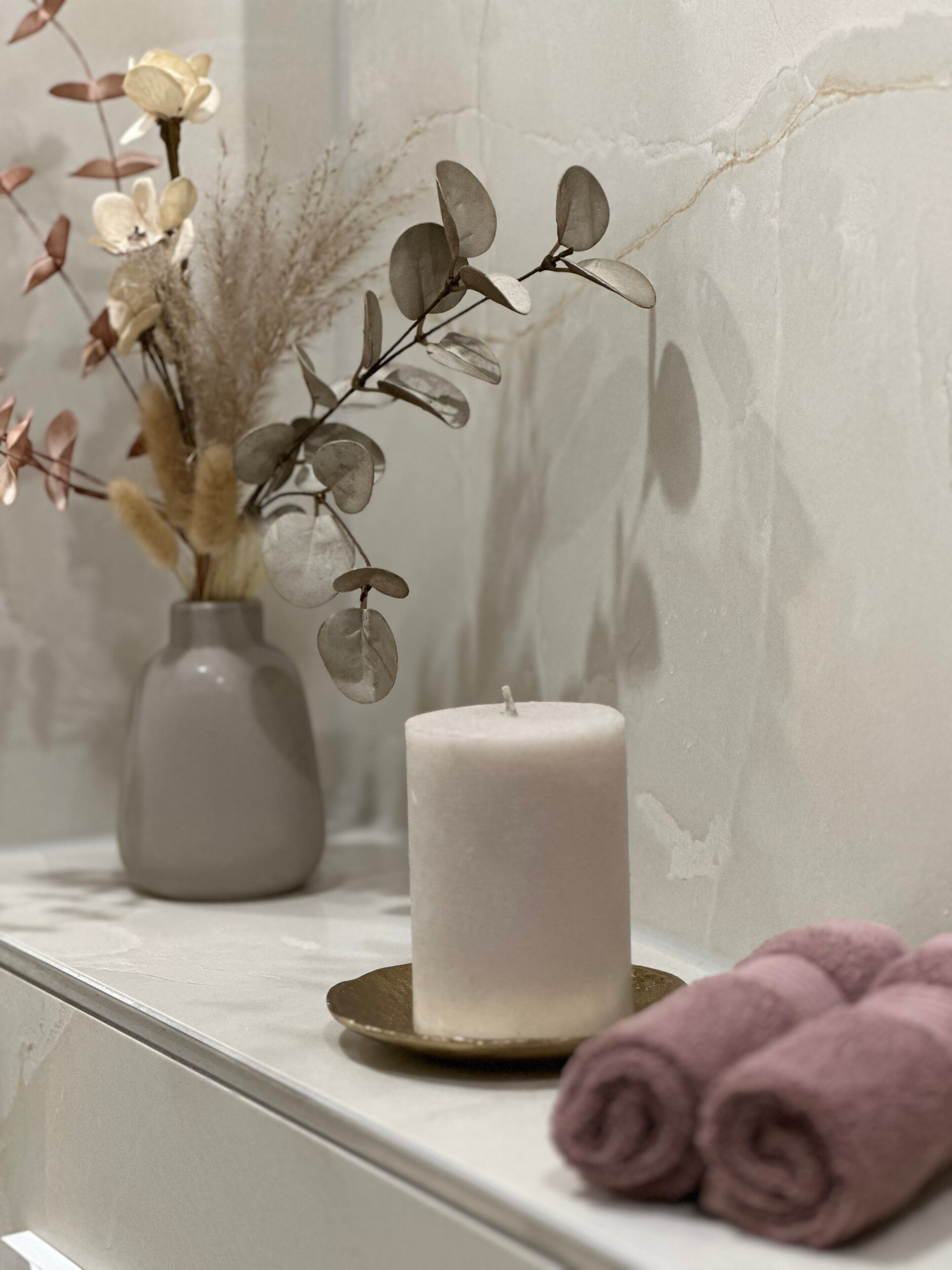 Un baño con una bañera blanca, una toalla blanca y un florero con flores secas.
