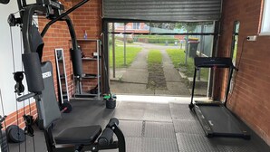 Une salle de sport équipée de matériel de musculation, d’un tapis de course et d’une porte donnant sur l’extérieur.