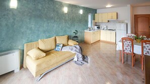 A living room with a sofa, a dining table with chairs, a kitchen area with cabinets and appliances, and a radiator. - Nice apartment in Stara Novalja with heated swimming pool (Stara Novalja)