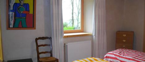 A room with a bed, a chair, a radiator, a window with curtains, and a painting on the wall.