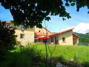 Ein zweistöckiges Haus mit einer Stein-Fassade, einem roten Ziegeldach und einer Terrasse mit Sonnenschirm.