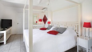 Habitació d'hotel amb un llit amb cortines, una televisió sobre un suport i un escriptori amb una làmpada.
