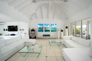 A spacious living room with white sofas, glass coffee tables, and a large flat-screen TV. - Encore   Tropical Gardens and Ocean Views (Saint Martin)