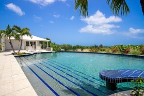 A swimming pool with clear blue water, a sun lounger, and a covered seating area. - Encore   Tropical Gardens and Ocean Views (Saint Martin)