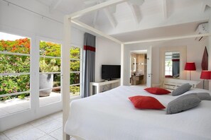 A bedroom with a bed, a TV, a desk, and a bathroom visible through an open door. - Encore   Tropical Gardens and Ocean Views (Saint Martin)