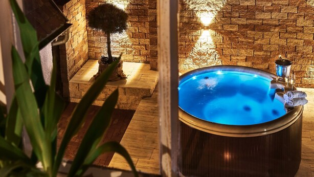 A spa area with a hot tub, wooden flooring, a stone wall, and a potted plant. - Holiday Home Lilace with Hot Tub, Fireplace, 4 Bedrooms, Max. 8 Guests (Böttingen)
