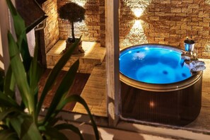 Wellnessbereich mit Whirlpool, Holzboden, Steinwand und einer Pflanze im Blumentopf.