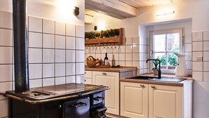 A kitchen with a stove, cabinets, a window, and a shelf with plants and kitchenware. - Holiday Home Lilace with Hot Tub, Fireplace, 4 Bedrooms, Max. 8 Guests (Böttingen)