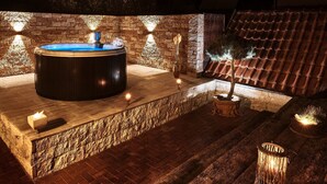 A hot tub with a stone wall backdrop, a potted tree, and a lantern on a wooden deck. - Holiday Home Lilace with Hot Tub, Fireplace, 4 Bedrooms, Max. 8 Guests (Böttingen)