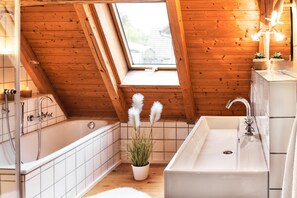 A bathroom with a skylight, a bathtub, a sink, and a potted plant. - Holiday Home Lilace with Hot Tub, Fireplace, 4 Bedrooms, Max. 8 Guests (Böttingen)