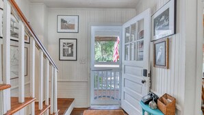 A hallway with a wooden staircase, a door leading outside, and a small table with a basket. - 4 Bedroom 2 Bath Inlet Front Home with Deep Water Access (Murrells Inlet)