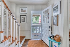 Un couloir avec un escalier en bois, une porte donnant sur l’extérieur et une petite table sur laquelle se trouve un panier.