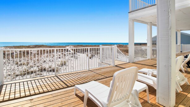 A wooden deck with white chairs and a railing overlooking the beach. - Coastal Luxury | Beachfront Home | Lagoon Views (Gulf Shores)