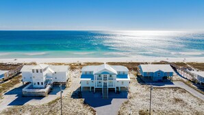 A beachfront property with multiple houses connected by a wooden walkway, overlooking a sandy beach and the ocean. - Coastal Luxury | Beachfront Home | Lagoon Views (Gulf Shores)