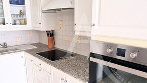 A kitchen with white cabinets, a granite countertop, a built-in oven, and a stove. - GRAND T2 AVEC TERRASSE, GARAGE ET PISCINE (Sète)