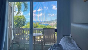 A room with a bed, a view of a balcony with a table and chairs, and a scenic view of a coastal area. - Queen Deluxe Double at Boundless Bliss Hotel (Southside)