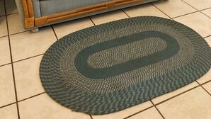 Un sofá azul claro con reposabrazos de madera y un tapete tejido verde oscuro sobre un suelo de baldosas.