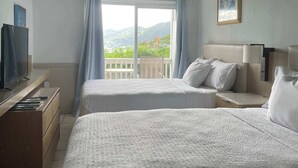 Ein Hotelzimmer mit zwei Betten, einem Deckenventilator, einem Fernseher und einem Balkon mit Bergblick.