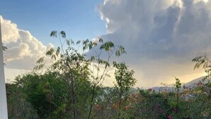 Ein Balkon mit rundem Tisch und zwei Stühlen, einem weißen Geländer und Blick auf einen Garten mit verschiedenen Pflanzen und Blumen.