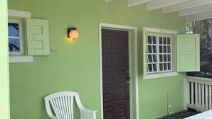 Eine Veranda mit einer grünen Wand, einer braunen Tür und zwei weißen Stühlen.