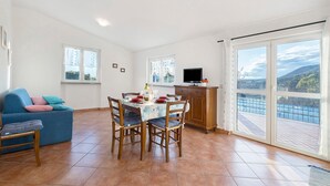 A dining area with a table set for four, a blue sofa, and a TV on a cabinet. - ‘Acacia’ Apartment with Sea View, Wi-Fi and Air Conditioning (Ceriale)