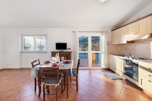 A kitchen with a dining table, chairs, a TV, and a view of the outdoors. - ‘Acacia’ Apartment with Sea View, Wi-Fi and Air Conditioning (Ceriale)