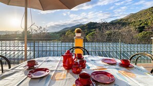 A table set for two with red tableware, a potted plant, and a view of a lake and hills. - ‘Acacia’ Apartment with Sea View, Wi-Fi and Air Conditioning (Ceriale)