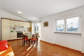 Una cocina con armarios blancos, una mesa de comedor con sillas, un sofá rojo y una ventana con vistas.